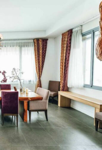 Bright dining room with patterned curtains, a wooden table, chairs, and a bench by the window.