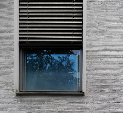 A window with closed blinds on a textured gray wall, reflecting trees.